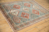 Angled view of a vintage Afshar rug with a distressed, geometric design in dusty blue and rust red.