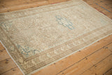 Angled view of a distressed Persian Mehriban rug showing its soft sand and dusty teal allover pattern.