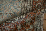 Distressed Tabriz rug shows a rust border folded over the dusty teal field with Herati motifs.