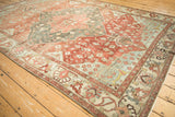 Distressed Baktiari carpet with faded floral vines and large-scale border patterns in red, teal.