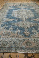 A long angle view across the low, distressed pile of a vintage Persian Veece carpet in denim blue and beige.
