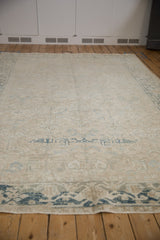 Distressed vintage Heriz carpet with worn beige pile, faded blue floral motifs and visible foundation.