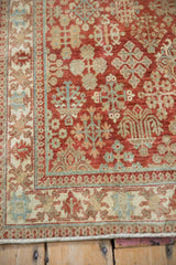 Corner of a distressed Joshegan rug showing the pawn design border and cherry red floral field.