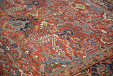 Vintage Heriz rug detail featuring brick red field with scrolled arabesque leaves and rich blue patterns.