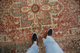 Distressed vintage Heriz carpet showing worn lattice vines and geometric patterns in ruby, blue.