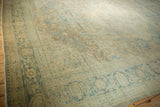 Corner of distressed Tabriz carpet with dusty blue palmette border and worn beige field.
