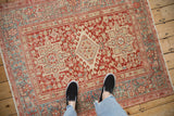 Standing on a distressed Persian Karaja rug, showing the cherry red and slate blue geometric field.