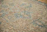 Distressed Heriz carpet displaying geometric blue blooms and scrolled vines on an ivory ground.