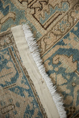 Distressed vintage Heriz carpet close-up, showing worn pile, secured edge, dusty blue, and beige.