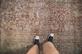 Overhead view of a distressed vintage carpet's low pile and floral border in raspberry and seafoam green.