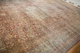 Angled view of heavy abrash across the faded floral field of a vintage distressed carpet.