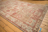Angled view of a distressed Baktiari carpet with repeating garden panels in red, powder blue, and sand tones.