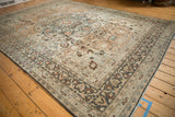 Angled view of a distressed vintage carpet detailing the charcoal vine border and worn sandalwood field.