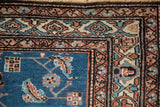 Corner detail of a vintage Persian rug with a geometric border in rust, ivory, and blue tones.