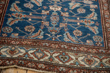 Corner view of a vintage Persian rug's geometric ivory border and sapphire blue Herati field.