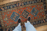 Overhead view of a vintage Heriz runner with three blue geometric medallions on a dusty brick red field.