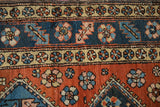 Hand-knotted Heriz rug runner showing floral pinwheel borders in dusty brick red, navy, and beige.