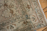 Distressed Khorassan rug corner with fringe, machine-bound side, and worn beige-blue floral pattern.