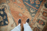 Standing on an antique Serapi rug, revealing the time-softened texture and geometric patterns in sandalwood and navy.