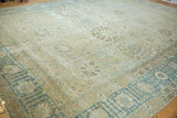 Angled view of a distressed Tabriz carpet highlighting the dusty blue border and worn beige field.