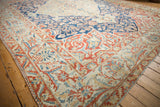 Corner of a distressed Baktiari rug with a low-pile floral border in shades of red, blue, and sand.