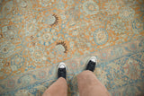A person's perspective looking down at the distressed, low-pile texture of a vintage Tabriz rug.
