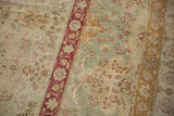 Distressed vintage Kerman carpet featuring Safavid floral motifs in faded red, ivory, and gold.