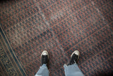 Feet on distressed antique Serbend carpet, showing worn aubergine field and faded navy boteh design.