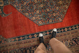 Angled view of an antique Bijar showing the abrashed red field and dusty teal Herati design spandrel.