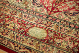 A pale green signature cartouche inside the cochineal red floral border of an antique Kerman rug.