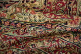 Folds of an antique Kerman rug revealing cochineal red and navy blue floral patterns.