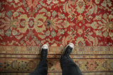 A standing view shows the distressed, low pile of a vintage Mahal carpet in red and saffron.