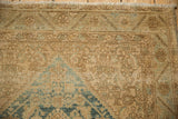 Close-up of distressed vintage Sarouk rug corner with faded beige, blue, and green serrated border.