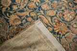 Distressed Kerman carpet corner showing worn floral arabesques, sapphire blue, and intact selvage.