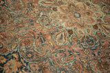 Vintage Kerman rug's intricate floral arabesque pattern in dusty rose, blue, and cream with visible wear.