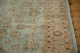 Corner view of a vintage distressed carpet showing its worn texture and floral border in brown and blue.