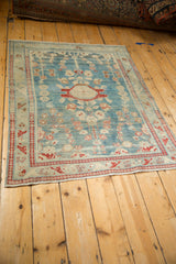 Corner of a distressed Persian Lilihan rug with cherry red arabesque border and intact ivory fringe.