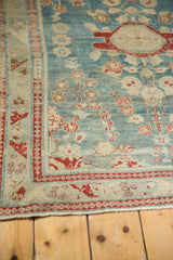 Distressed Lilihan rug corner with intact fringe, cherry red arabesque border on sky blue.