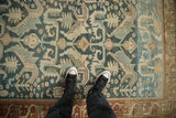 A person's perspective of the worn, geometric patterns on a vintage dusty teal and ivory Mehreban rug.