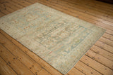Distressed corner of a vintage Hamadan rug, highlighting soft blue, ivory, and rust botanical patterns.