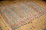 Angled view of a distressed Kurdish rug with a blue and red allover lattice pattern and heavy abrashes.