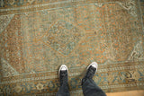 Person's view of the scale and distressed texture of a vintage terracotta and blue rug.