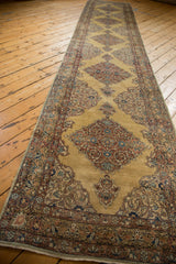 Lengthwise perspective of a Kerman rug runner with diamond medallions on an ochre gold field.