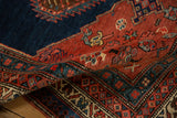 A folded corner of an antique Persian Bijar rug showing its dense pile and geometric border patterns.