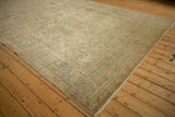Angled perspective on the distressed texture and scrolled floral border of a vintage Kerman carpet.