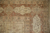 Distressed vintage Tabriz carpet corner with faded floral motifs in beige, ivory, and chestnut rust.