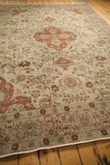 Angled view of a distressed Tabriz carpet showing its low pile and sprawling vine design.