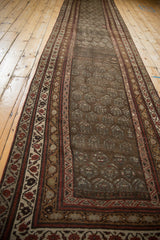 Angled view of distressed vintage Kurdish runner, showcasing tribal geometric borders and faded boteh motifs.