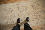 Distressed vintage Oushak runner with light beige field, muted geometric pattern, foundation showing.