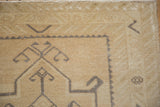 Distressed vintage Oushak rug corner, showing light beige pile, geometric pattern, faint foundation.